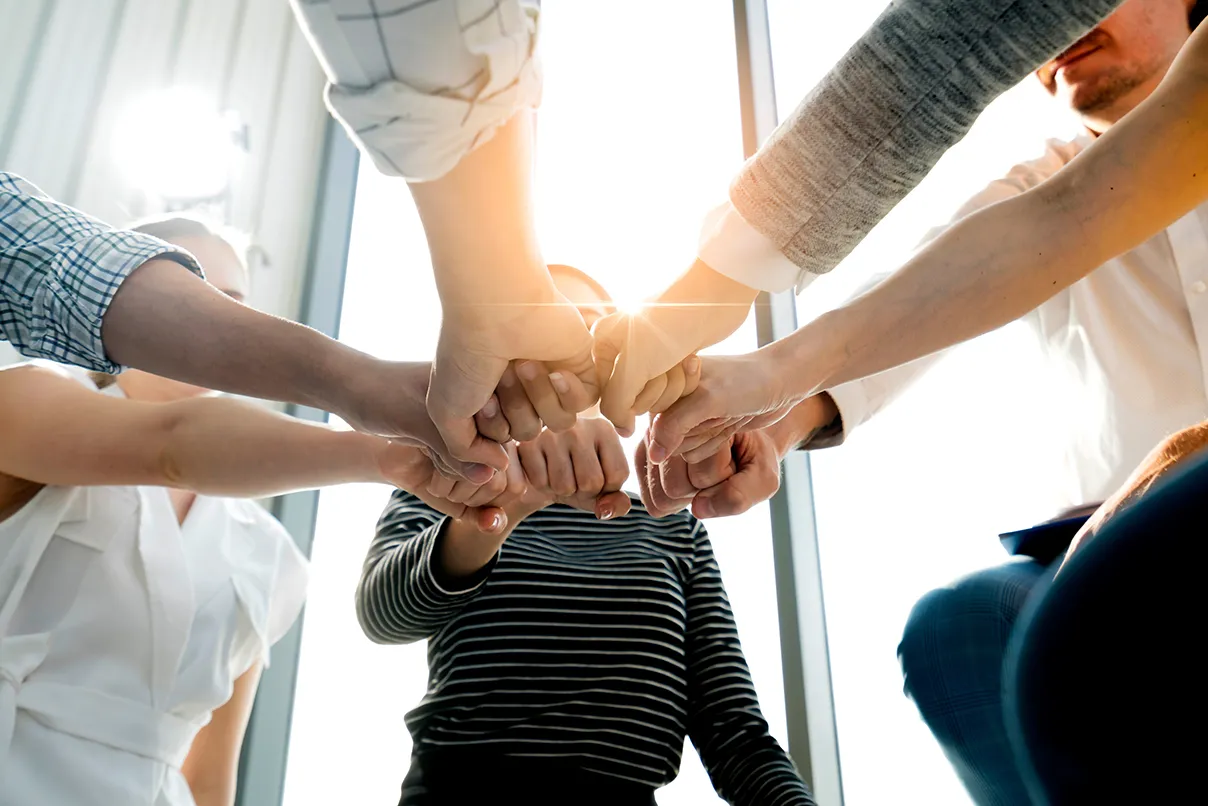 Team members share a group fist bump in a sunlit workspace, representing trust, teamwork, and the harmony of AI and culture in staffing.